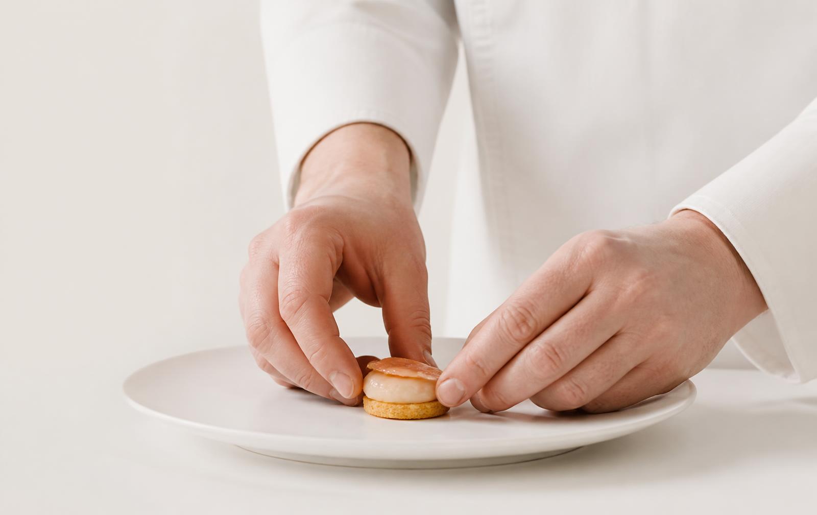 Le chef dresse à la pince des bouchées apéritives sur un plan de travail en marbre